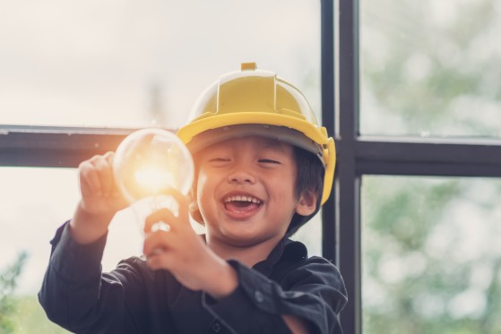 A child wearing a safety helmet holds a light bulb.