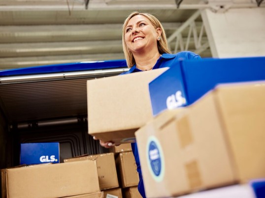 Smiling man siting with a parcel in a warehouse of colourful garden gnomes.