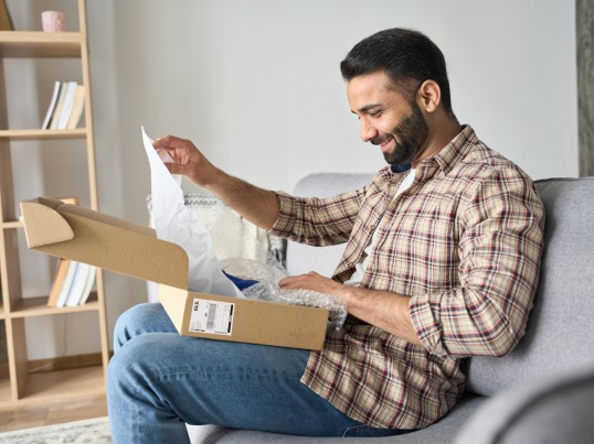 Man sitting on the couch opening a box delivered by GLS