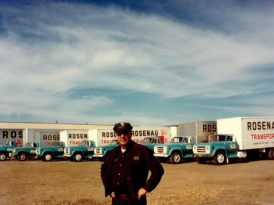 Man standing in front of Rosenau trucks in a yard in the 1950s.