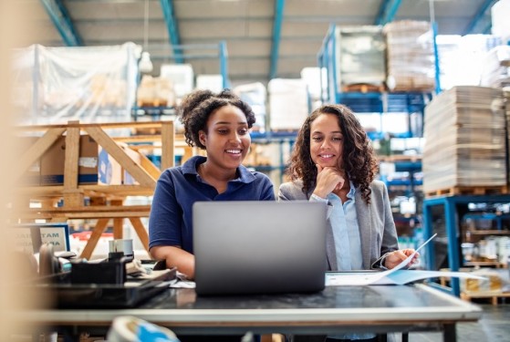 Two women in a warehouse with a laptop
