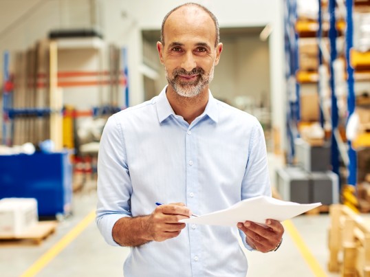 Man in a warehouse holding paper sheet and pencil