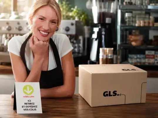 Smiling shopkeeper at a parcel shop counter with a GLS parcel box.