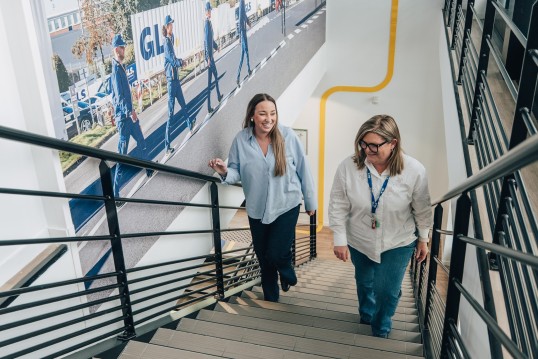 Female colleagues in a logistics company office, walking up a staircase together as a team.