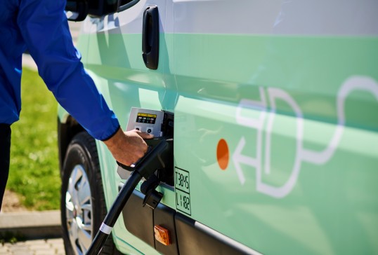 Electric utility van plugged into a charging station, illustrating lower-emission delivery.