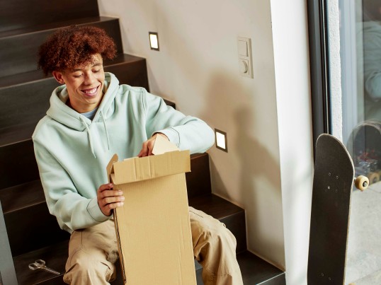 Young man sitting on stairs and opening a parcel